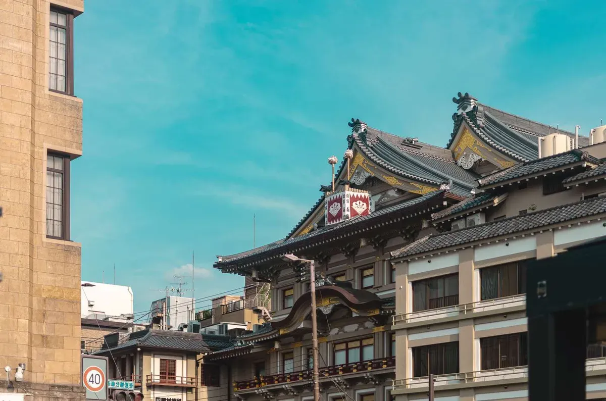 Traditional tiled-roof theatre building in Kyoto's Gion district under a blue sky, near a geisha dinner show venue