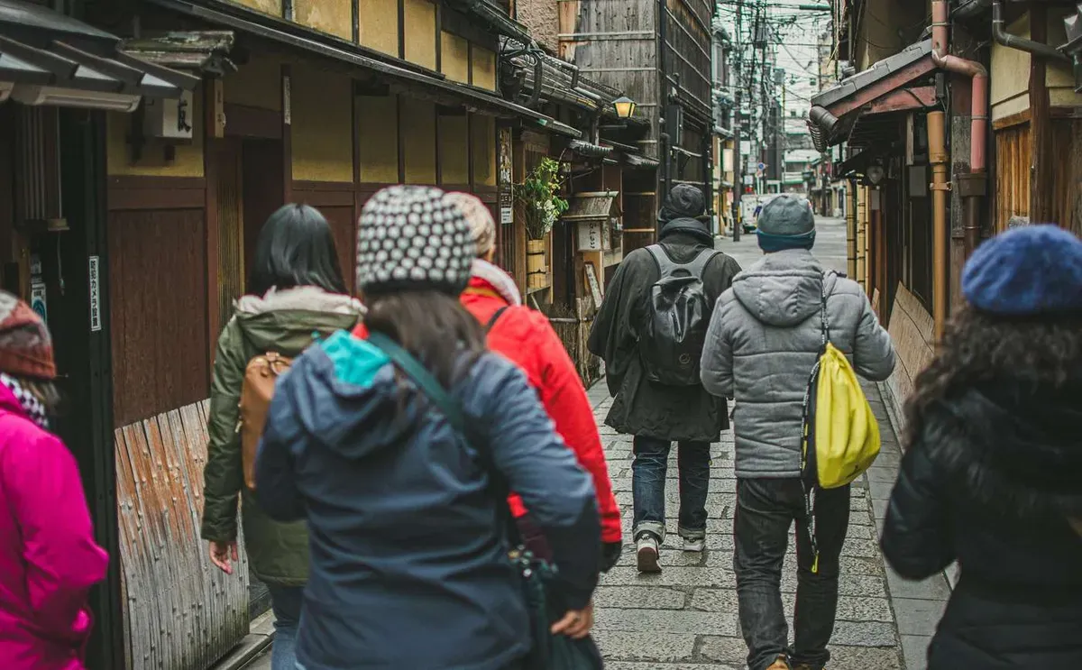 Small group on a guided walking tour down a traditional wooden machiya lane in Kyoto's Gion geisha district before a geisha dinner show