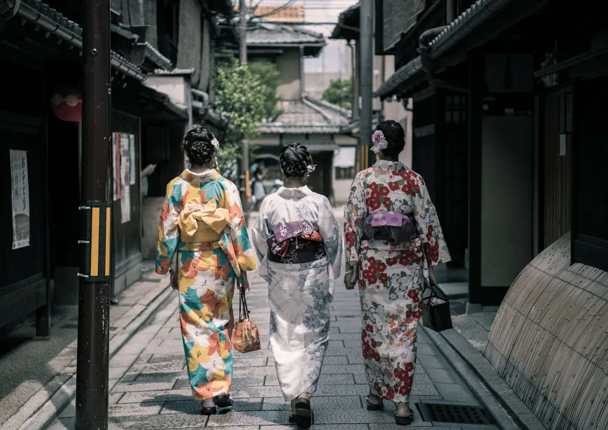Three visitors in colorful kimono walking down a traditional lane in Kyoto's Gion geisha district