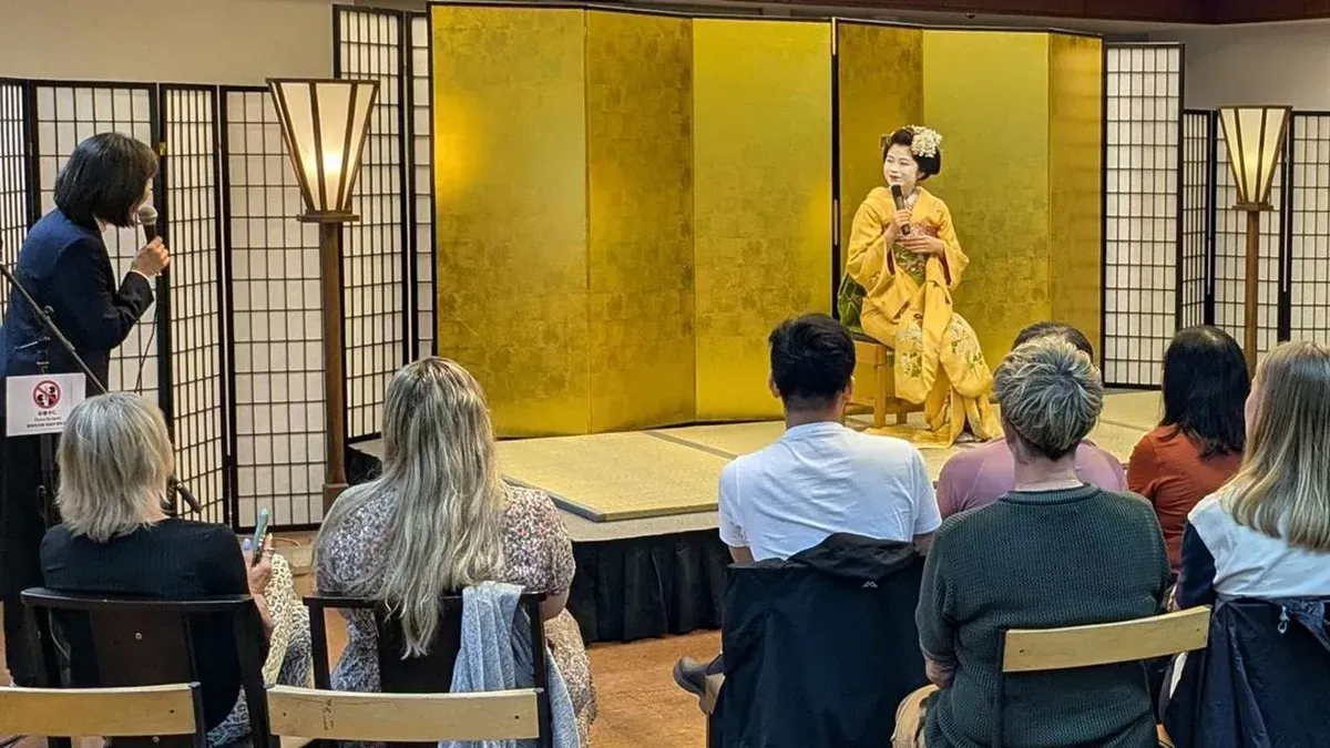 Maiko in a golden kimono answering questions through an interpreter during a meet-and-greet maiko show in Kyoto