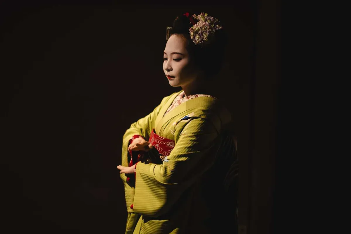 Apprentice maiko in a green kimono with floral kanzashi performing a short dance at a maiko meet-and-greet in Kyoto