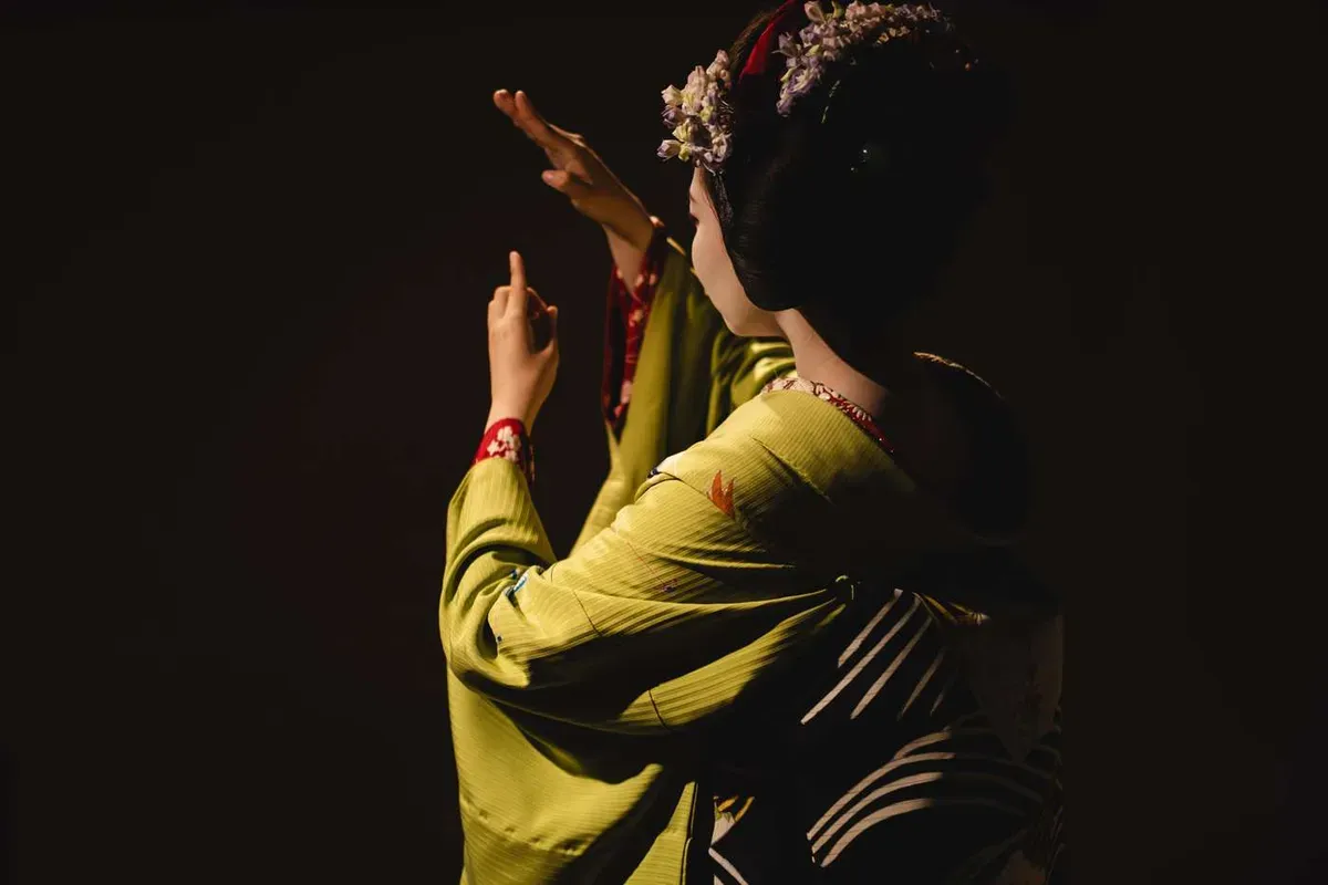Maiko in a green kimono raising her arms in a traditional dance pose at a private geisha performance in Kyoto