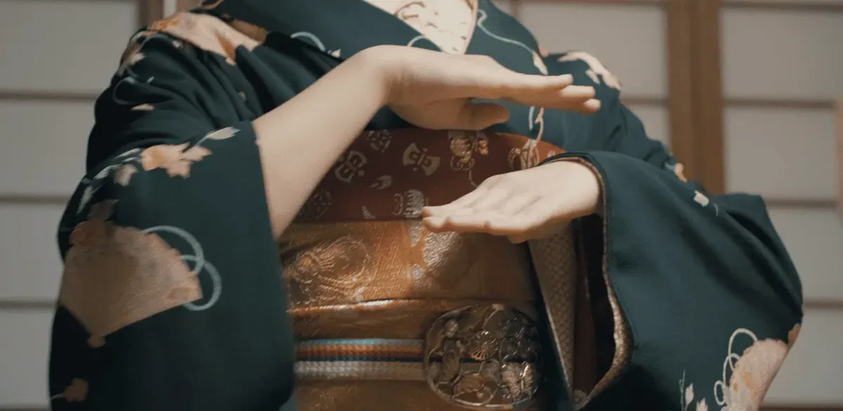 Close-up of a geiko in an embroidered kimono and ornate obi performing a hand gesture at a geisha show in Kyoto's Gion district, Japan