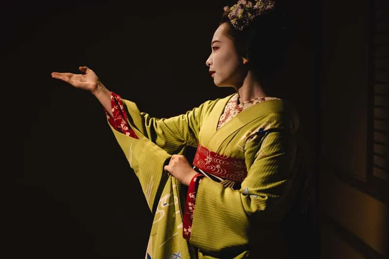 Apprentice maiko in red kimono performing a traditional dance at a private geisha show in Kyoto, Japan