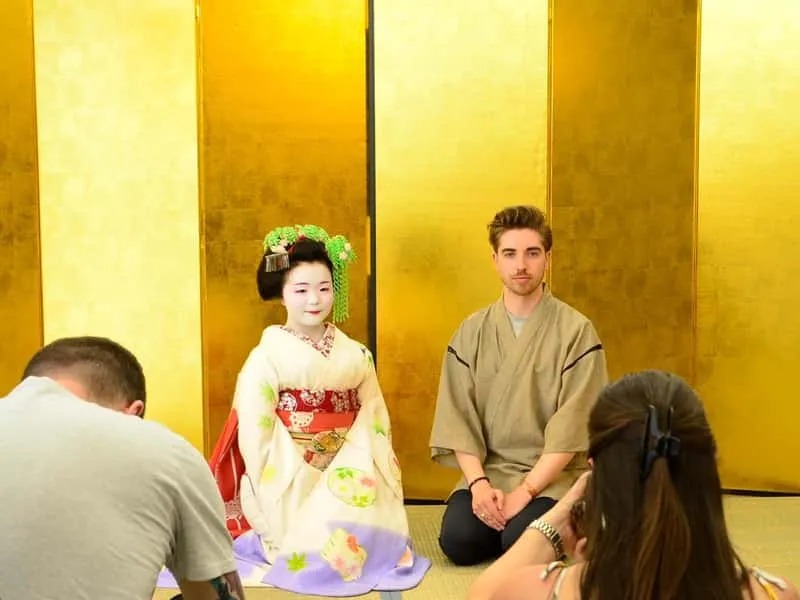 Maiko in elaborate hairpins greeting smiling guests at an intimate maiko show and geisha experience in Kyoto, Japan